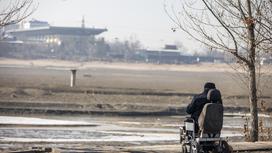 Мужчина сидит на коляске возле озера Сайран