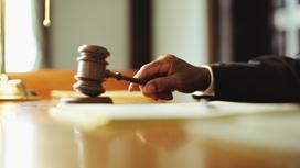 Судья держит в руке судейский молоток, опущенный на стол