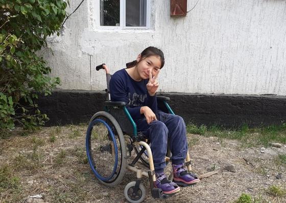 Девочка сидит в инвалидном кресле возле дома Девочка сидит в инвалидном кресле возле дома