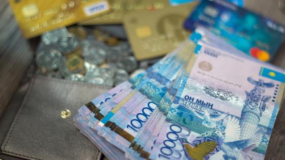 Пачка тенге лежит на кошельке среди монет и банковских карт Пачка тенге лежит на кошельке среди монет и банковских карт