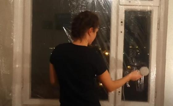 Женщина утепляет окно термопленкой Женщина утепляет окно термопленкой