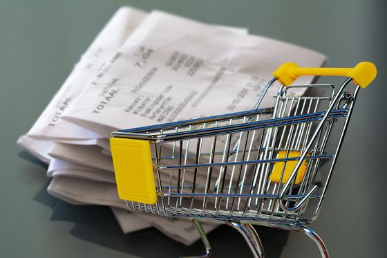 Крзина для покупок стоит на фоне стопки чеков Крзина для покупок стоит на фоне стопки чеков