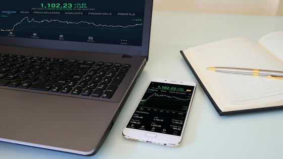 Телефон с программой для инвестирования лежит на столе рядом с блокнотом Телефон с программой для инвестирования лежит на столе рядом с блокнотом