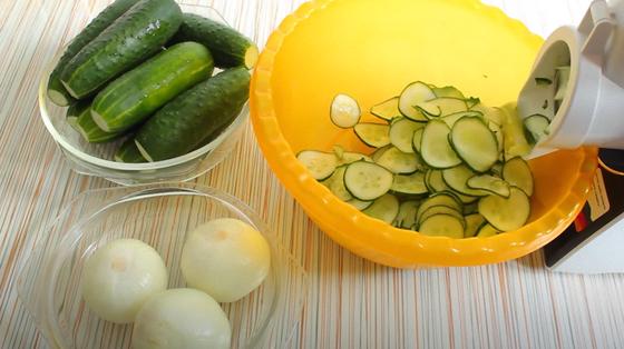 Огурцы, лук и кухонный комбайн с нарезанными кружочками огурцов Огурцы, лук и кухонный комбайн с нарезанными кружочками огурцов