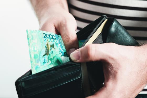 Мужчина держит в руках кошелек с одно купюрой в 2000 тенге Мужчина держит в руках кошелек с одно купюрой в 2000 тенге