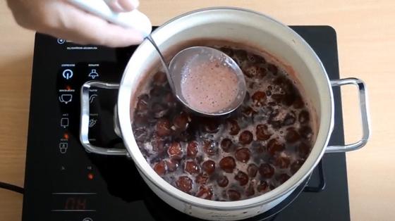 Ложкой снимают пену с черешен, кипящих в кастрюле Ложкой снимают пену с черешен, кипящих в кастрюле