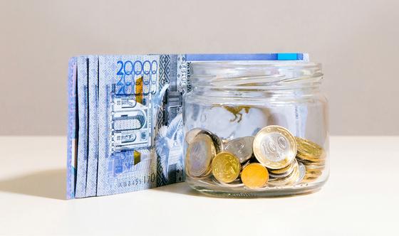 Купюры тенге лежат рядом с банкой монет Купюры тенге лежат рядом с банкой монет