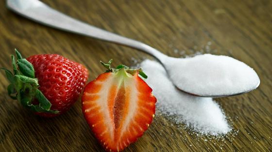 На столе ложка с сахаром и разрезанные ягоды клубники На столе ложка с сахаром и разрезанные ягоды клубники
