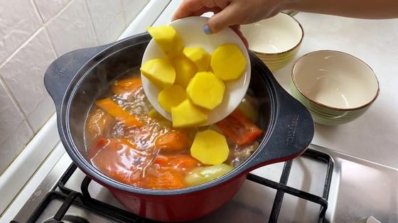 Добавление картошка в кастрюлю с бульоном Добавление картошка в кастрюлю с бульоном