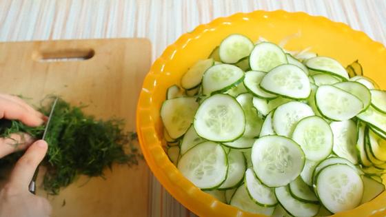 Миска с кружочками огурцов и лука и ножом нарезают укроп Миска с кружочками огурцов и лука и ножом нарезают укроп