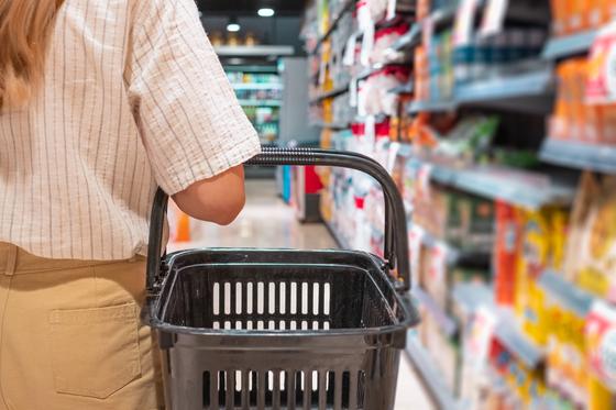Девушка стоит с продуктовой корзиной рядом с полкой в супермаркете Девушка стоит с продуктовой корзиной рядом с полкой в супермаркете