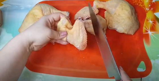 Женщина разрезает по суставам крылья и бедра курицы Женщина разрезает по суставам крылья и бедра курицы