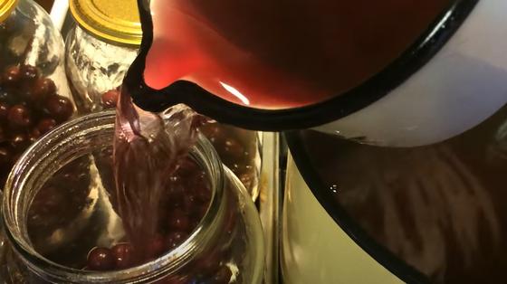 Кружкой набирают сироп с кастрюли и заливают в банку с вишнями Кружкой набирают сироп с кастрюли и заливают в банку с вишнями