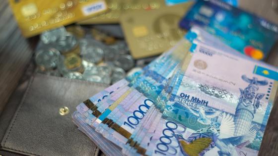 Пачка тенге лежит на кошельке среди монет и банковских карт Пачка тенге лежит на кошельке среди монет и банковских карт