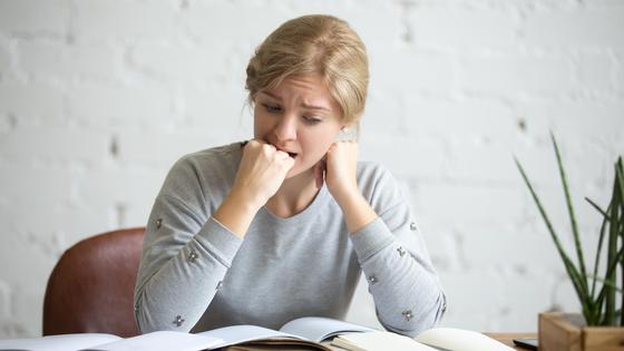 Девушка кусает кулак за столом с книгами Девушка кусает кулак за столом с книгами