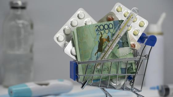 Лекарства и деньги лежат в миниатюрной тележке для покупок Лекарства и деньги лежат в миниатюрной тележке для покупок