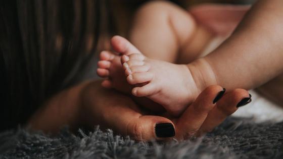 Женщина с накрашенными ногтями держит ножки малыша в руках Женщина с накрашенными ногтями держит ножки малыша в руках