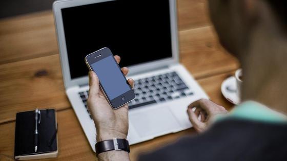 Мужчина держит в руке смартфон, на фоне ноутбук Мужчина держит в руке смартфон, на фоне ноутбук