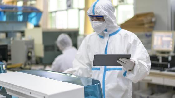 Медик в защитном костюме и с планшетом в руке стоит у медоборудования в больнице Медик в защитном костюме и с планшетом в руке стоит у медоборудования в больнице