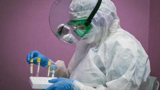 Медик в защитном костюме берет пробирку из подставки Медик в защитном костюме берет пробирку из подставки
