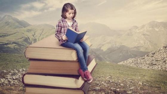 девочка сидит на стопке книг и читает девочка сидит на стопке книг и читает