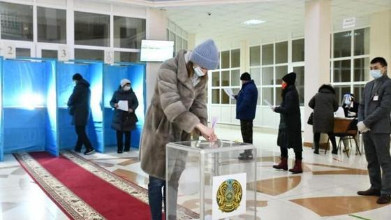 Женщина в куртке бросает бюллетень в урну Женщина в куртке бросает бюллетень в урну