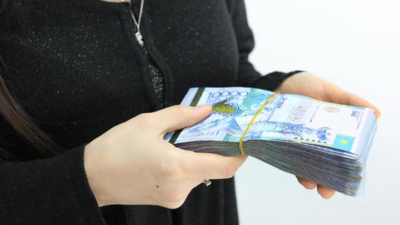 Женщина держит пачку купюр номиналом 10 тысяч тенге Женщина держит пачку купюр номиналом 10 тысяч тенге