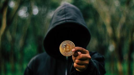 Мужчина в капюшоне держит монету с изображением логотипа биткоина Мужчина в капюшоне держит монету с изображением логотипа биткоина
