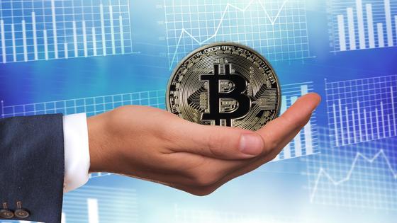Мужчина держит в руке биткоин на фоне графиков Мужчина держит в руке биткоин на фоне графиков