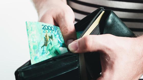 Мужчина держит в руках кошелек с одно купюрой в 2000 тенге Мужчина держит в руках кошелек с одно купюрой в 2000 тенге
