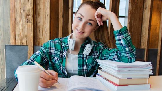 Девушка за столом с книгами и конспектами Девушка за столом с книгами и конспектами