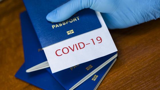 Рука в перчатке держит паспорт с листком, на котором написано "COVID-19" Рука в перчатке держит паспорт с листком, на котором написано "COVID-19"
