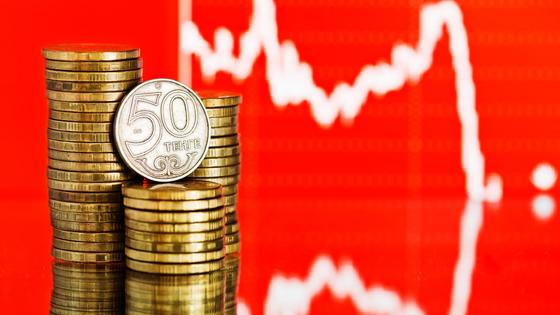 Монеты тенге лежат стопкой на фоне графика Монеты тенге лежат стопкой на фоне графика