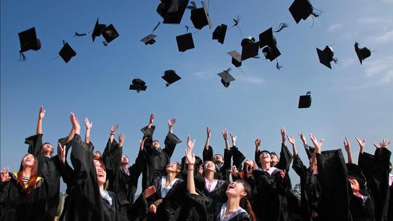 Студенты-выпускники в мантиях подбрасывают в небо головные уборы Студенты-выпускники в мантиях подбрасывают в небо головные уборы