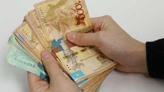 Человек держит пачку тенге в руках Человек держит пачку тенге в руках