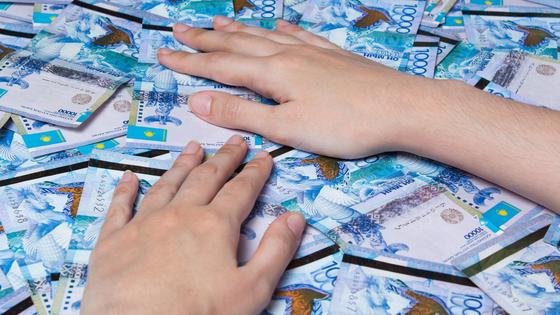 Мужчина загребает руками купюры тенге Мужчина загребает руками купюры тенге