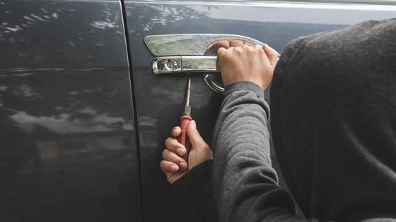 Человек взламывает дверь авто отверткой Человек взламывает дверь авто отверткой