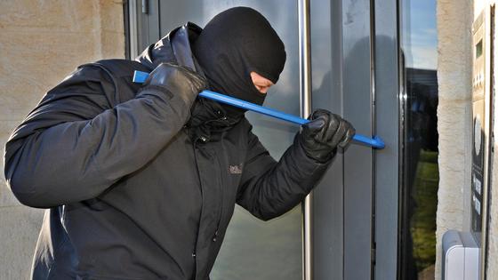 Мужчина в черном взламывает дверь с помощью монтировки Мужчина в черном взламывает дверь с помощью монтировки