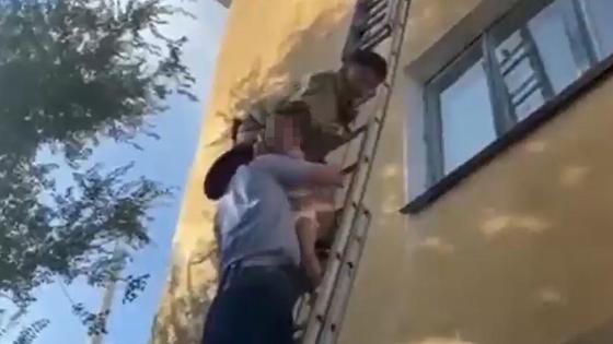 Спасатель передает ребенка полицейскому на лестнице Спасатель передает ребенка полицейскому на лестнице