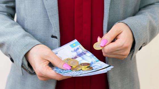 Женщина держит в руках купюры и монеты тенге Женщина держит в руках купюры и монеты тенге