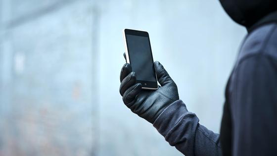 Мужчина в черной одежде и в перчатках держит в руке смартфон Мужчина в черной одежде и в перчатках держит в руке смартфон