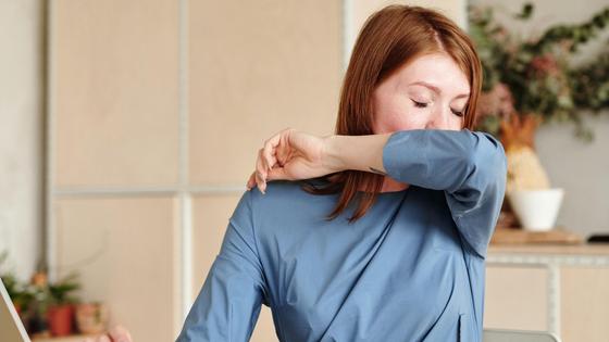 Девушка кашляет за столом в локоть Девушка кашляет за столом в локоть