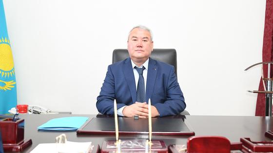 Серикжан Ерекешев сидит за столом на рабочем кресле Серикжан Ерекешев сидит за столом на рабочем кресле