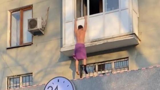 Мужчина висит на балконе в розовом полотенце и одном носке Мужчина висит на балконе в розовом полотенце и одном носке
