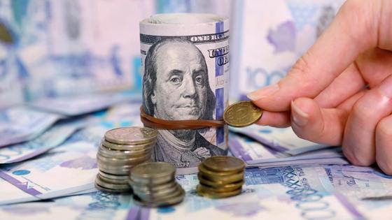 Женщина сравнивает монеты тенге с пачкой долларов Женщина сравнивает монеты тенге с пачкой долларов
