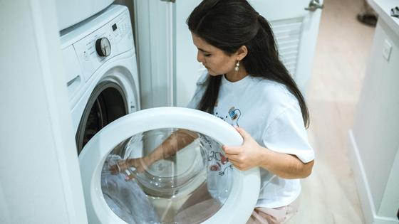 Девушка кладет вещи в стиральную машинку Девушка кладет вещи в стиральную машинку