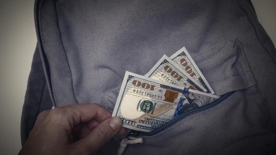 Рука вытаскивает банкноты из серого рюкзака Рука вытаскивает банкноты из серого рюкзака