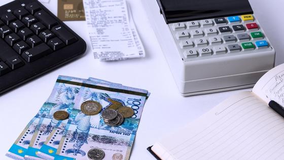 Тенге лежат рядом с чеками, кассовым аппаратом и блокнотом Тенге лежат рядом с чеками, кассовым аппаратом и блокнотом